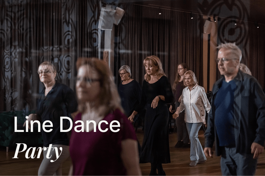 Gruppe von Erwachsenen beim Line Dance in einem Saal mit Vorhängen und gedimmtem Licht
