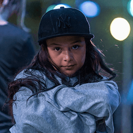 Junges Mädchen mit schwarzer Baseballcap und grauem Hoodie bei Nacht mit verschwommenen Lichtern im Hintergrund