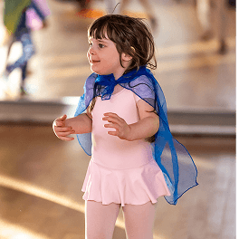 Kleines Mädchen in rosa Ballettkleidung mit blauem Chiffon-Schal tanzt in heller Tanzstudioumgebung