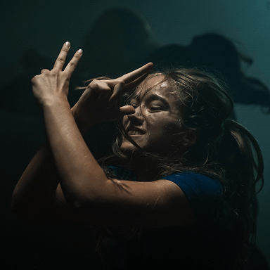 Junge Frau mit blonden Haaren in blauer Kleidung tanzt mit geschlossenen Augen vor dunklem Hintergrund