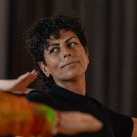 Porträt einer Person mit kurzen lockigen Haaren und dunkelgrünem Rollkragenpullover vor dunklem Vorhang