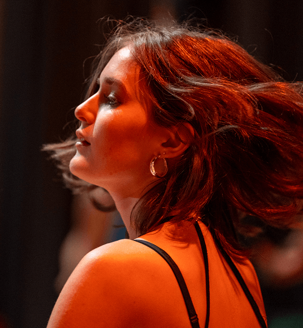 Seitliches Porträt einer jungen Frau mit rotbraunen Haaren und goldenen Creolen vor dunklem Hintergrund